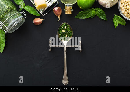 Sauce Pesto dans une cuillère vintage avec des ingrédients : les pignons de pin, basilic vert, l'ail, parmesan, huile d'olive sur fond de ciment noir foncé. Recette italienne Banque D'Images