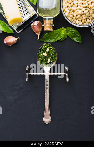 Sauce Pesto dans une cuillère vintage avec des ingrédients : les pignons de pin, basilic vert, l'ail, parmesan, huile d'olive sur fond de ciment noir foncé. Recette italienne Banque D'Images