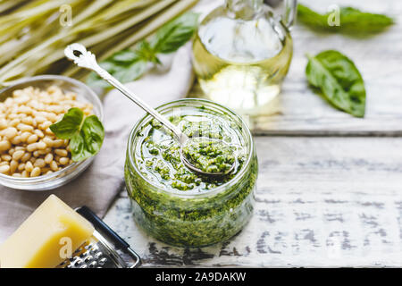 Fettuccine au pesto vert et sauce à la cuillère sur le verre vintage pot de sauce pesto avec des ingrédients sur la table rustique en bois blanc. Pesto italien traditionnel Banque D'Images