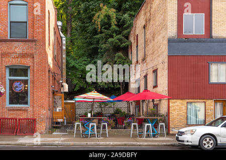 Un petit café terrasse avec parasols colorés est pris en sandwich entre deux bâtiments de brique dans la ville historique de Wallace, de l'Idaho. Banque D'Images
