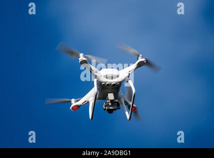 Drone blanc sur ciel bleu avec hélices tournants. Banque D'Images