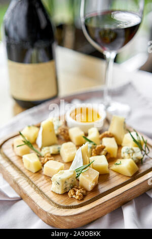 Plaque de bois avec du fromage. Vin rouge sur fond de verre . Mélange de fromages délicieux avec des noix, du miel. Plat de dégustation sur une plaque de bois. La nourriture pour le vin. Banque D'Images