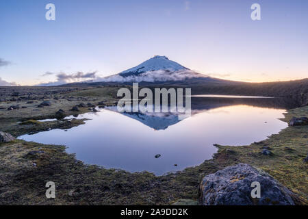 Les sommets enneigés du volcan Cotopaxi reflétée dans le paisible lac Santo Domingo pendant la lueur de coucher du soleil. Banque D'Images