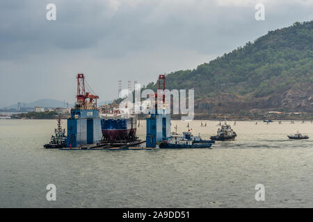 Vung Tau, Vietnam - 12 mars 2019 : cale sèche flottante bleu avec à l'intérieur du navire et plusieurs remorqueurs à proximité, sur la mer de Chine du Sud verdâtre bleu en cloudsc Banque D'Images