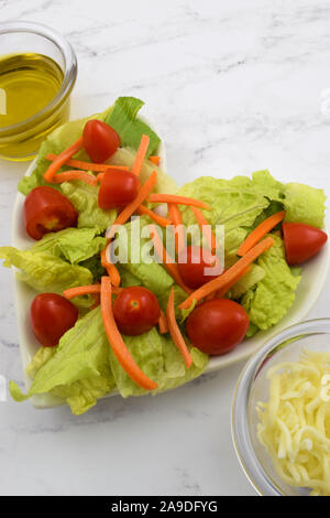 Coeur frais salade saine sur une plaque en forme de coeur avec la laitue romaine, de carottes, de tomates, d'huile d'olive et du fromage râpé. Fait avec amour. Banque D'Images