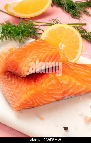 Tranches de saumon au citron et aneth, close-up avec sel et poivre, la cuisson du poisson, sur un fond rose Banque D'Images