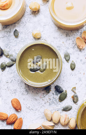 Le beurre de noix et graines en pots avec des ingrédients. Des matières d'amande bio, noix de cajou, pistaches, noix de macadamia coller et graines de citrouille beurre sur un onglet Banque D'Images