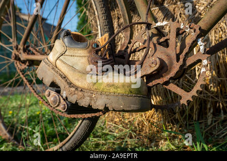 Vieille paire de chaussures de randonnée en cuir usé sur un rusty vintage bicycle outdoors en équilibre sur les pédales comme si il équitation Banque D'Images