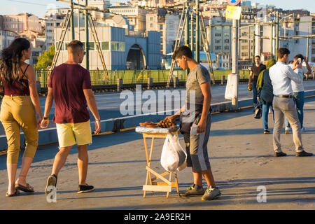 6e 2019 Turkey-September,Istanbul. Un jeune vendeur vend des aliments frits sucrés pâtisseries au passant sur le pont de Galata en fin d'après-midi, soleil de l'été Banque D'Images