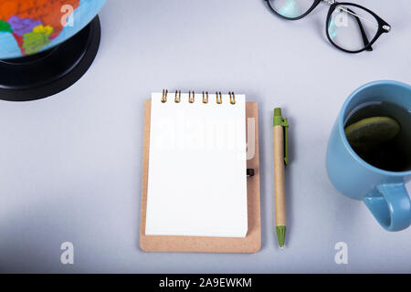 Bloc-notes avec stylo, lunettes de lecture, globe et une tasse de thé sur la table gris. Haut veiw Banque D'Images