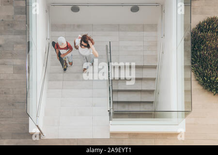 Mère et fils branchés sur des escaliers à pied dans un contexte de centre-ville moderne. Jeune garçon avec skateboard va vers le haut de l'échelle avec maman. Vue supérieure de personnes marche dans un Banque D'Images