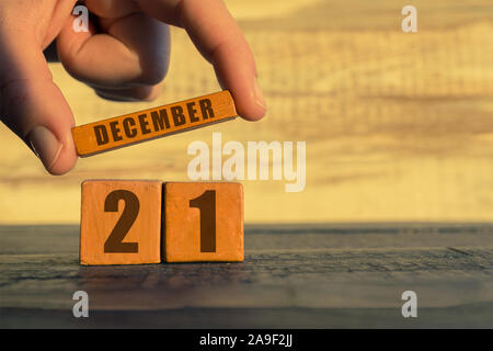 Au 21 décembre. Jour 20 de mois, calendrier sur un cube de bois. a woman's hand met le nom du mois sur le nombre de mois sur un fond de bois Banque D'Images