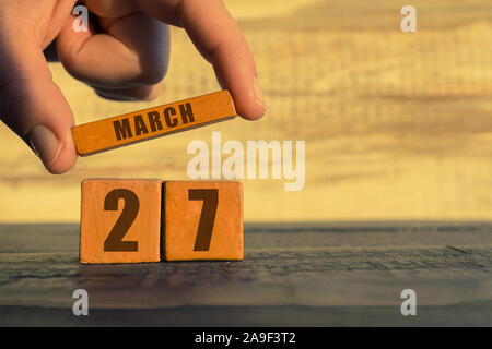 Le 27 mars. Jour 27 du mois, calendrier sur un cube de bois. a woman's hand met le nom du mois sur le nombre de mois sur un fond de bois sp Banque D'Images