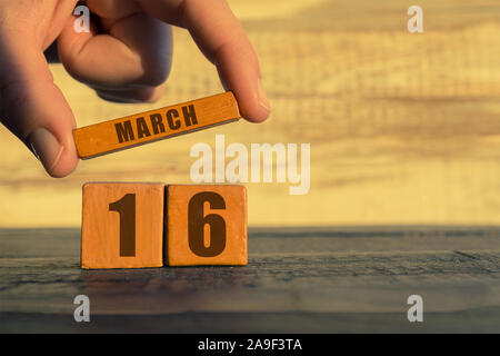 16 mars. Jour 16 de mois, calendrier sur un cube de bois. a woman's hand met le nom du mois sur le nombre de mois sur un fond de bois sp Banque D'Images