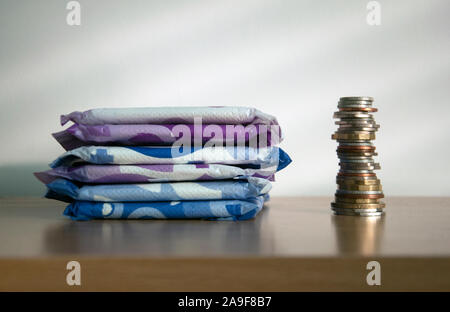 Une pile de serviettes à côté d'une pile de pièces de grande taille. Illustrant la pauvreté et période unaffordability de matériel sanitaire pour de nombreuses femmes dans le monde Banque D'Images