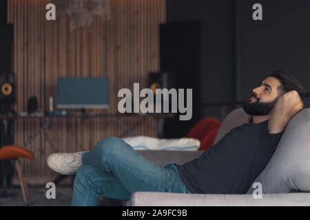 Young attractive guy relaxant assis sur un canapé dans son bureau loft Banque D'Images