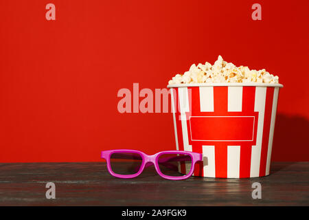 Lunettes 3d et godet à rayures avec popcorn contre fond rouge Banque D'Images