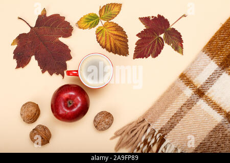 Sécher les feuilles jaune et marron, tasse de café, de noix, de pomme et de Plaid à carreaux sur le fond beige. Un thème d'automne. Vue d'en haut. Banque D'Images