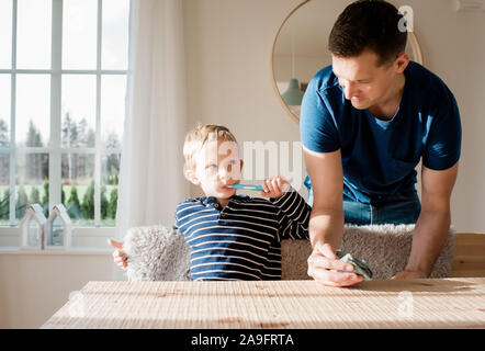 Jeune garçon se brosser les dents en regardant son père avant de l'école Banque D'Images