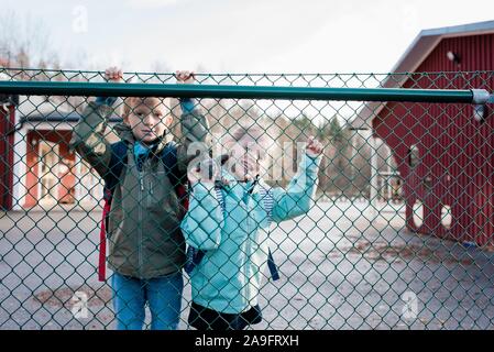 Frères et sœurs à la clôture de l'école à travers un sourire à papa. Banque D'Images