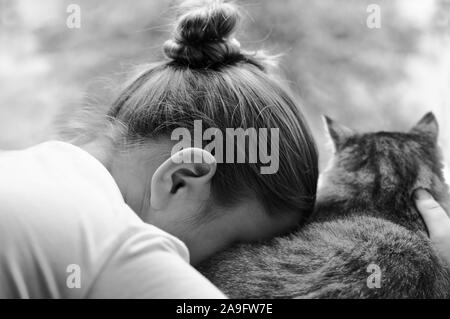 Triste fille avec un chat est assis avec son dos à la caméra. La jeune fille appuya sa tête contre le chat.offensé enfant. Image en noir et blanc.L'horizontale. Banque D'Images