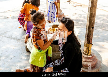 Un enfant s'applique Thanaka (écran solaire naturel) sur le visage d'un adulte, la Pagode Kuthodaw, Mandalay, Myanmar. Banque D'Images