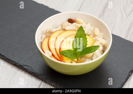 Avec Bol en porcelaine avec de la bouillie de sorgho peach, noix de cajou et amandes sur conseil de pierre. Sans gluten vegan salade de sorgho avec des fruits frais. Banque D'Images