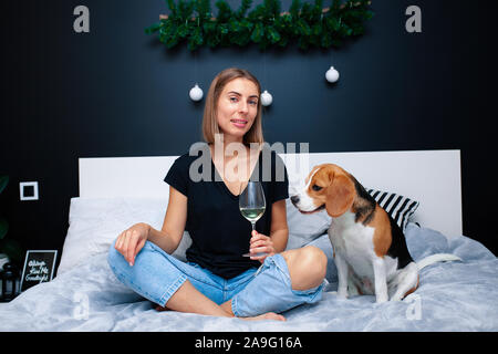 Belle Jeune femme jouant avec chien assis sur le lit dans une chambre élégante. Les animaux domestiques à la maison. Chien Beagle. L'amitié. Confort confort Banque D'Images