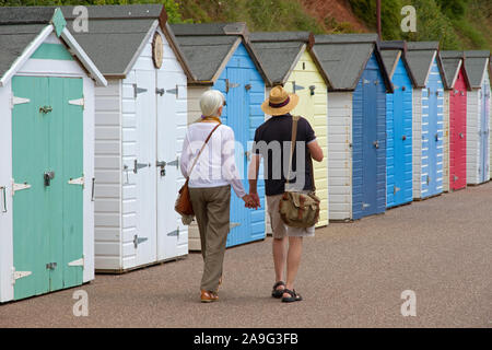 Couple walking cours des cabines de plage, promenade, Seaton, Devon, England, UK Banque D'Images