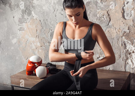 La boxe. Boxer femme assis sur un banc rétractable bandage autour de main pensive Banque D'Images