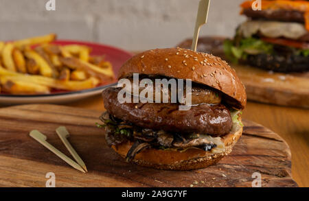Délicieux petit hamburger au foie poilé, champignons, salade et sauce de veau sur planche de bois Banque D'Images