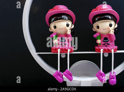Figurines en céramique de deux jeunes filles en robe rose sur un fond noir. Banque D'Images