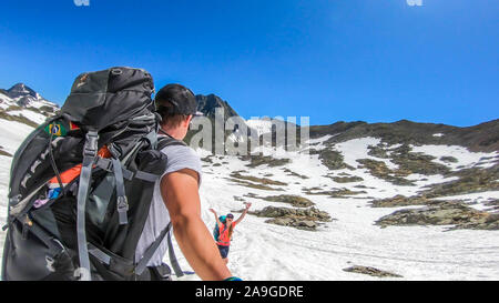 Un couple avec de grands sacs à dos promenades sur la pente enneigée en haute montagne. Alpes Schladming, Autriche. La jeune fille saute autour, être heureux. L'homme est taki Banque D'Images