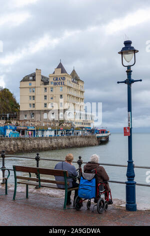 Deux femmes matures, l'un en fauteuil roulant, s'asseoir sur la promenade de Llandudno surplombant le Grand Hôtel en automne Banque D'Images