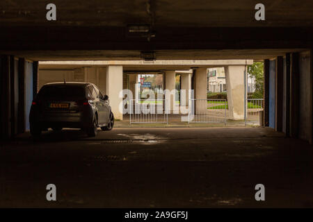 Voiture individuelle garée dans un garage souterrain sombre à Queensway Estate, Southend. Des éclaboussures de lumière provenant de l'extérieur, encadrant des piliers en béton et des clôtures. Banque D'Images