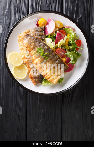 Filet de loup de mer au plat de service avec une salade de légumes frais et de citron libre sur une plaque sur la table. Haut Vertical Vue de dessus Banque D'Images