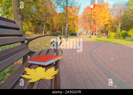 Dans le parc, les feuilles mortes se trouvent sur un chemin et sur banc en bois avec cahier rouge. Journal signet est à partir de feuilles d'érable. Dans l'arrière-plan sont yello Banque D'Images