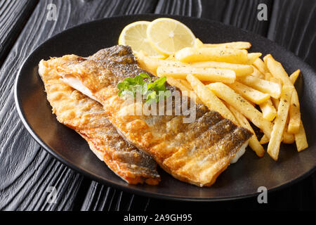 Menu de poêlée de filet de loup de mer au citron et frites sur une assiette sur la table horizontale. Banque D'Images