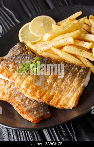 Filet de loup de mer grillé avec frites gros plan sur une plaque verticale sur la table. Banque D'Images