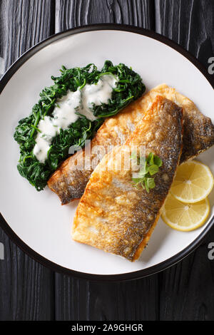 Filet de loup de mer grillé servi avec du citron, épinards et sauce crémeuse libre sur une plaque sur la table. Haut Vertical Vue de dessus Banque D'Images