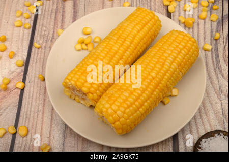 Deux épis de maïs bouillis dans une assiette, le maïs en grains et le gros sel sur la table. Régime alimentaire sain. Régime alimentaire de remise en forme. Pour une petite douceur Banque D'Images