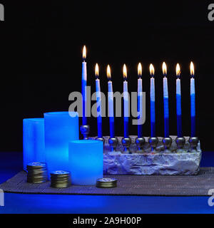 Hanouka still life de bleu des bougies électriques, Menorah et des piles de pièces d'or Banque D'Images