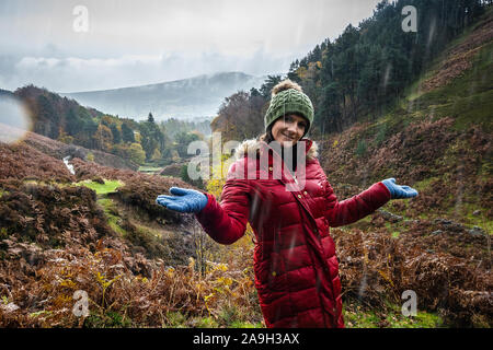 Une jeune femme, randonneur, alpiniste prend une pause dans l'ascension d'une montagne et de pose pour une photo tout en se tenant dans la pluie froide d'hiver Banque D'Images