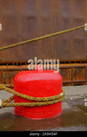 Corde d'un navire attaché à un vieux bollard d'amarrage en béton rouge sur un quai. Banque D'Images