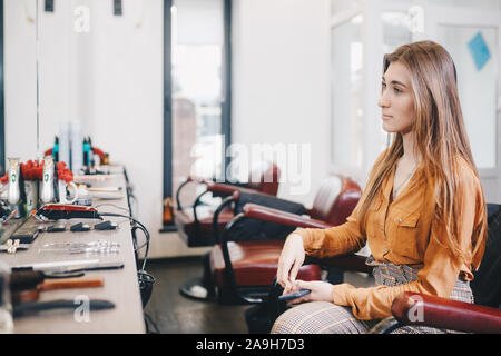 Cliente en chaise à en miroir d'un salon de coiffure. Client attend son styliste en beauté tout en restant assis dans la chaise de coiffure Banque D'Images