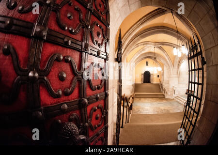 Portes cerclées de fer dans la crypte de la Cathédrale nationale de Washington | WASHINGTON — Une imposante porte rouge cerclée de fer s’ouvre sur un couloir en pierre voûté dans la crypte de la Cathédrale nationale de Washington, à Washington, D.C. Le fer forgé clouté et les charnières surdimensionnées rappellent l’artisanat médiéval, faisant partie d’une structure en pierre porteuse construite sans squelette en acier entre 1907 et 1990. Le passage mène vers la chapelle de Saint-Joseph d’Arimathée dans la crypte et un escalier montant au niveau principal de la cathédrale. Banque D'Images