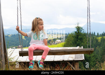 Petit enfant girl sitting on swing avec les montagnes derrière Banque D'Images