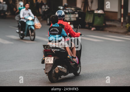 Hanoi, Vietnam - 18 octobre 2019 : Les parents prennent leurs enfants à l'école sur une mobylette dans les rues animées de Hanoi sans aucune protection ou un casque Banque D'Images