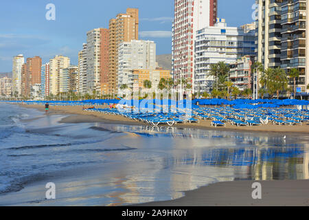 Benidorm ville et plage de Playa Levante, tôt le matin avec l'homme de marcher sur la plage et des réflexions dans le sable humide Banque D'Images