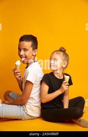 Drôle Les enfants mangent de la crème glacée à la vanille dans un cornet gaufré sur fond jaune, joyeux, frère et soeur Banque D'Images